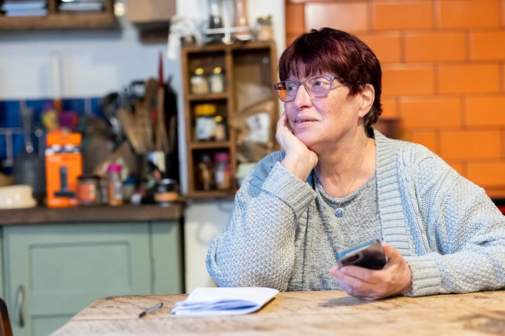 Idosa sentada à mesa da cozinha olhando o celular